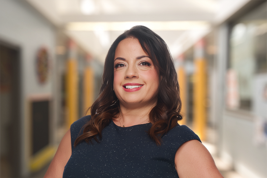 Photo of Amaris Rivas standing in front of a school hallway background