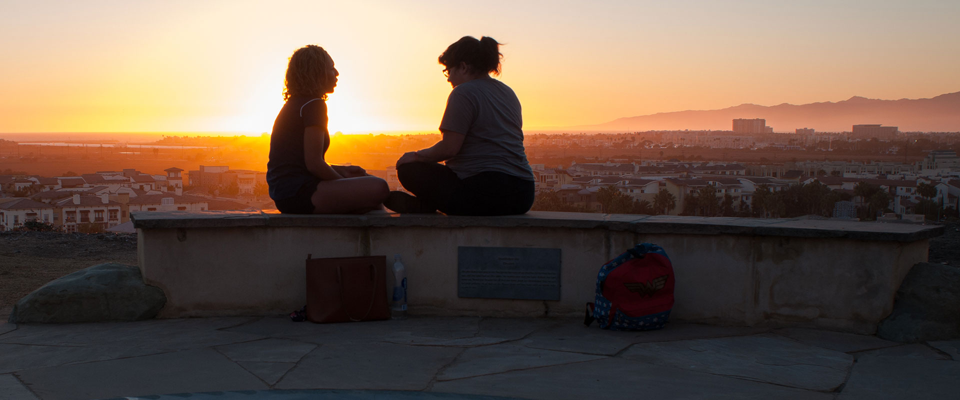 Two students sitting at the Tongva Memorial with the sun setting in the distance