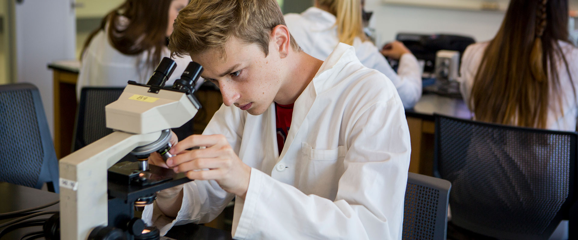 A student wearing a lab coat looking through a microscope